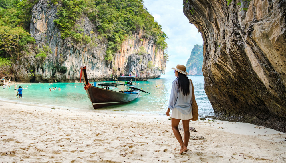Visitors enjoy the crystal-clear waters of Koh Hong Island, surrounded by towering limestone cliffs and lush greenery. A Thai women traveler relaxes on the soft sand of Koh Lao Lading Island Thailand